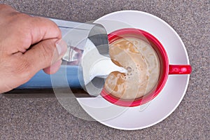 Hand of a man pouring milk into black coffee