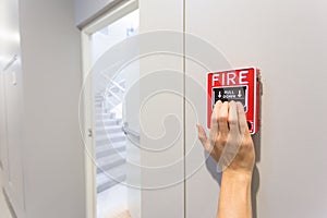 The hand of man is pulling fire alarm on the wall next to the do
