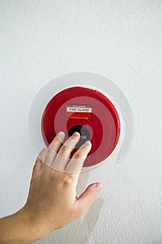 The hand of man is pushing fire alarm on the wall.