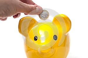 hand of man putting euro coin under yellow piggy bank