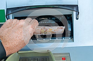 The hand of a man receiving turkish lira from an ATM on a clear day