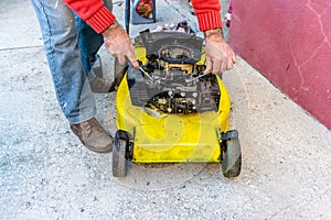 Hand of man repairing old grass cutter with tools on cement floor. Repairing lawn mower engine