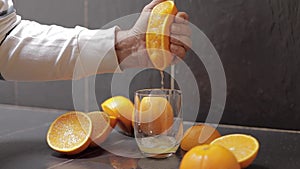 Hand of man squeeze juice from an orange into glass. Man hold half of orange on hand