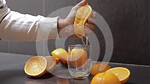 Hand of man squeeze juice from an orange into glass. Man hold half of orange on hand