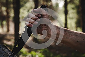 Hand of a man with a survival knife in his hands in the forest. Focus on the knife.