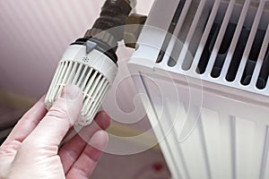 Hand of a man turning the radiator thermostat to a minimum with the coming of spring and warming in the apartment on the backgroun