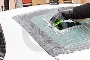Hand of man using green scraper to remove ice from window in car, winter problems