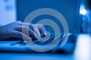 Hand of a man using laptop computer for hacking or steal data at night in office