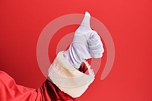 Hand of a man wearing santa claus costume and gloves over red background doing successful approval gesture with thumbs up,