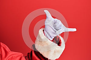 Hand of a man wearing santa claus costume and gloves over red background gesturing hawaiian shaka greeting gesture, telephone and