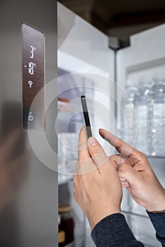 The hand of the man who controls the refrigerator with his smartphone. Internet of Things Concept