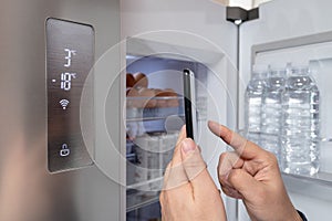 The hand of the man who controls the refrigerator with his smartphone. Internet of Things Concept