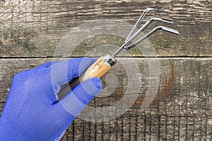 Hand of a man in a work glove with a garden rake on the background of an old wooden table