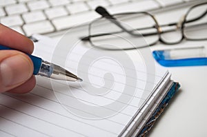 Hand of man writing with blue pen on spirales notebook on white desk background