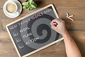 Hand man writing New year goals 2020 text on black board