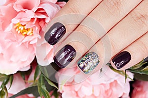 Hand with manicured nails colored with dark purple nail polish and pink peony flower