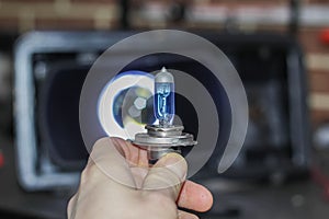 The hand of the master holds a halogen light bulb against the background of the car.