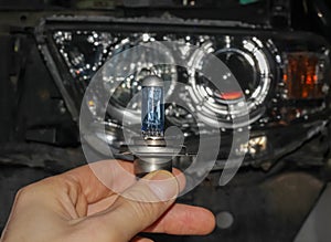 The hand of the master holds a halogen light bulb against the background of the car.