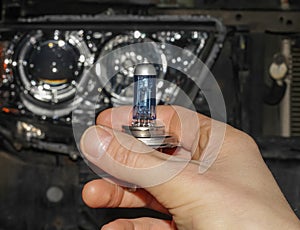 The hand of the master holds a halogen light bulb against the background of the car.