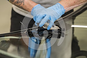 Hand from a mechanic with blue nitril gloves handling the camera and other equipment mounted on a front windshield of a car.