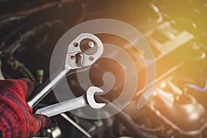 Hand of mechanic professional man hold a wrench tools with car engine blurred background in vehicle repair garage.