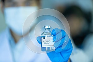 Hand in medical blue gloves holding a bottle of COVID-19 coronavirus vaccine