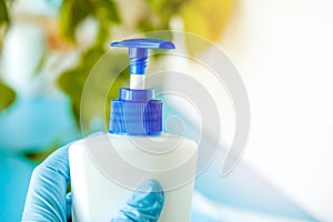 hand in a medical glove holds a bottle with an antiseptic on a background of green sheets and a white background, hygiene product,