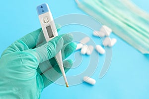 Hand in a medical glove holds a thermometer on blue background.