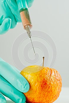 A hand in a medical glove inserts a syringe into apple. Harmful food additives. GMOs Concept