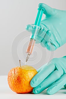 A hand in a medical glove inserts a syringe into apple. Harmful food additives. GMOs Concept