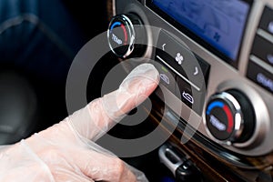 A hand in a medical glove presses the air recirculation button in the car