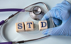 A hand in a medical glove puts cubes with the abbreviation STD on the background of a stethoscope