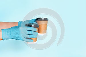 Hand in medical gloves carrying paper cup of takeaway coffee on blue background. Banner with copy space. Contactless delivery