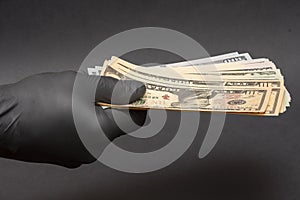 A hand in a medical rubber glove holds out a wad of dollars, selective focus, close-up. Concept: cash payment during the coronavir