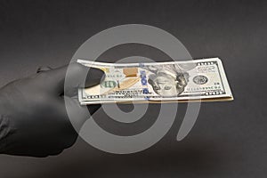 A hand in a medical rubber glove holds out a wad of dollars, selective focus, close-up. Concept: cash payment during the coronavir