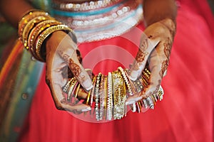 The hand with mehndi of Indian bride holding a lot of glitter bracelets bangle with red legenha background, close-up