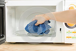 Hand with microfiber cleaning rag wiping inside of microwave oven,