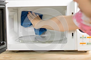 Hand with microfiber cleaning rag wiping inside of microwave oven,