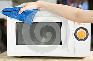 Hand with microfiber cleaning rag wiping inside of microwave oven,