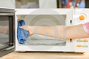 Hand with microfiber cleaning rag wiping inside of microwave oven,