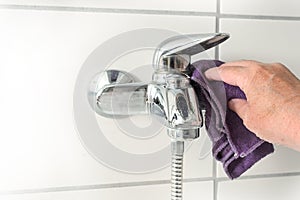 Hand with a microfiber cloth cleaning an old bathtub faucet full of limescale stains caused by hard calcium water, copy space,
