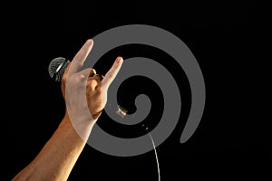 Hand with microphone and devil horns isolated on black