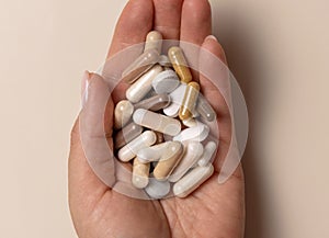 Hand with mix of medical capsules on light beige top view. Taking dietary supplements