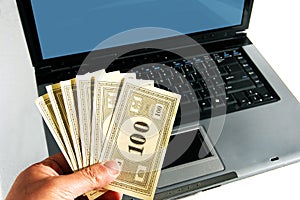 A hand with money in front of a computer