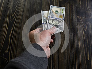 Hand with money on a wooden background. hand holding two 100 dollars banknote. US dollars in man hand