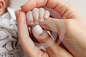 The hand of a mother and father close-up holds the fist of a newborn baby.