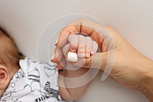 The hand of a mother and father close-up holds the fist of a newborn baby.