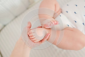The hand of the mother holds her plump legs baby, close up