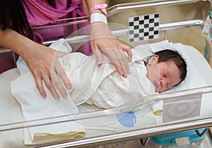 Hand of mother putting newborn baby to sleep in the infant bassinet basket at hospital