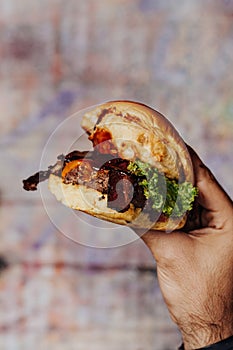 Hand with mouth-watering bacon and angus beef burger flavored with crunchy fried onion, adding freshly cut potato fries on the sid